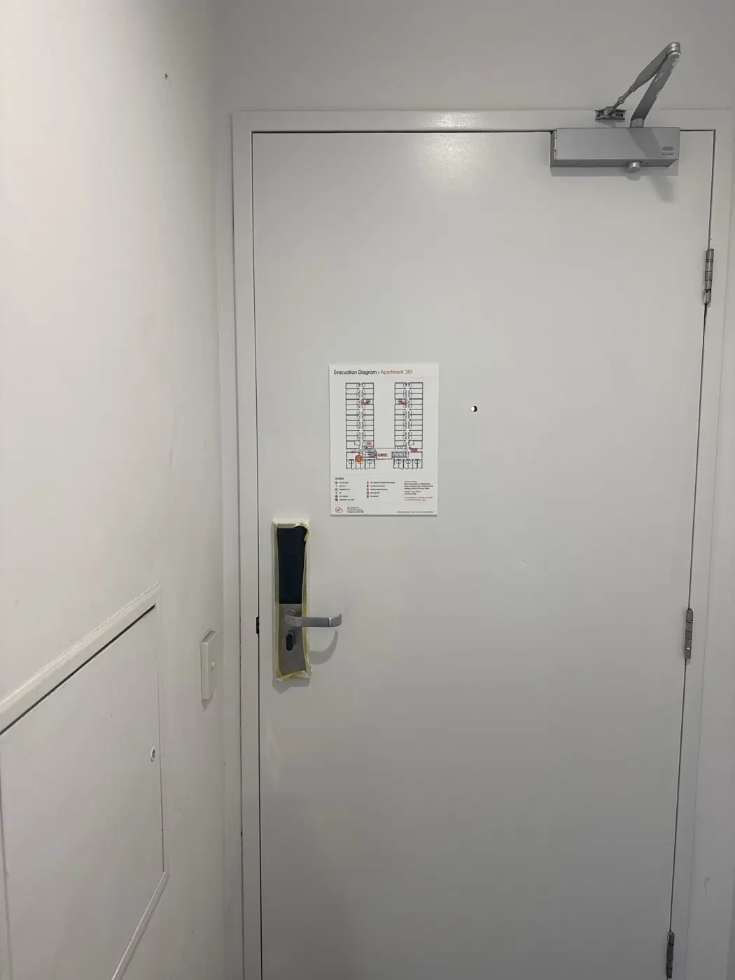 Evacuation diagram panel installed on a white apartment door with a door closer at Iglu Central Park