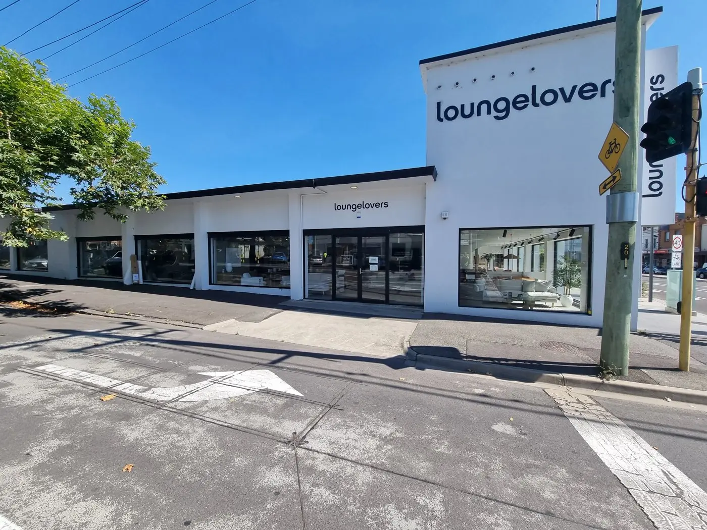 Wide view of a white Lounge Lovers showroom building with Birthday Sale panels along its window line