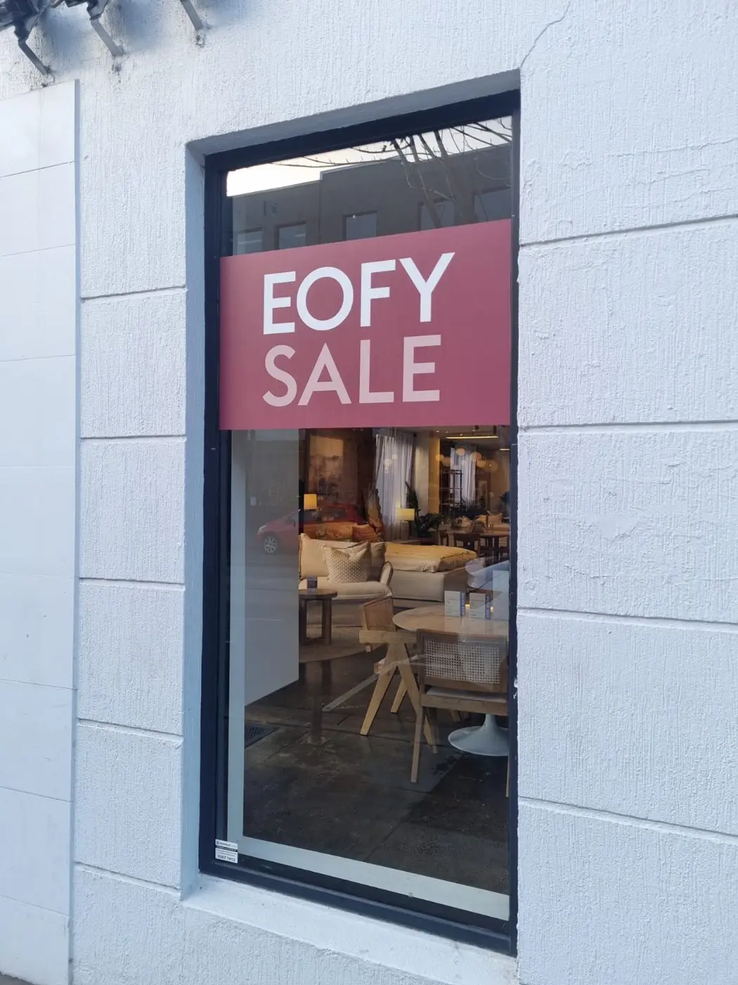 Vertical EOFY sale graphic at a glass entry door with the showroom interior visible behind