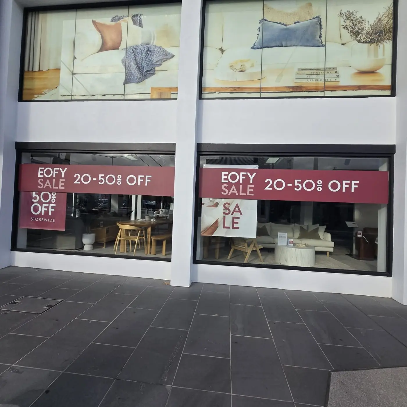 Two showroom windows with EOFY sale banners beneath large furniture lifestyle graphics