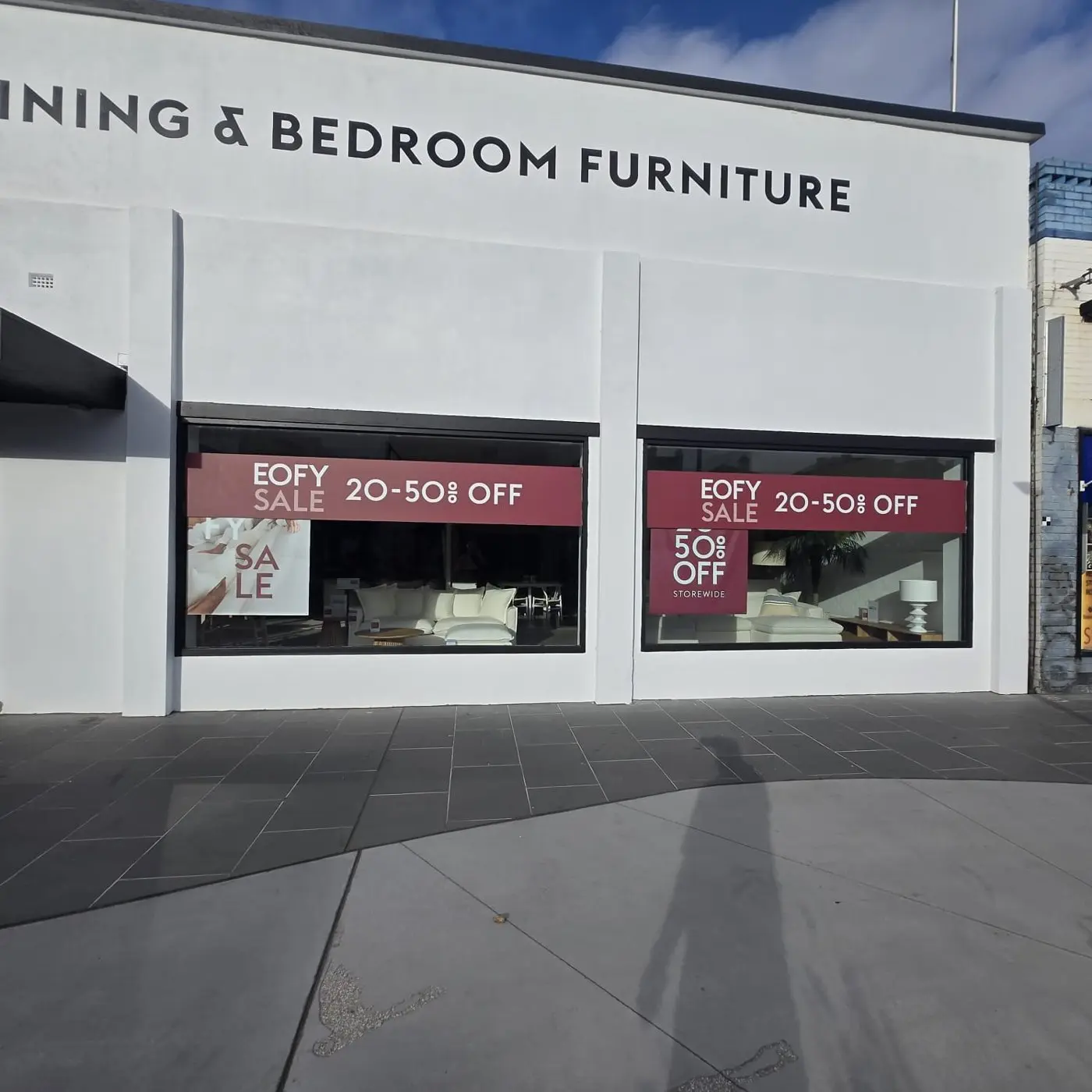 Showroom corner with dining and bedroom furniture building lettering above EOFY sale window banners