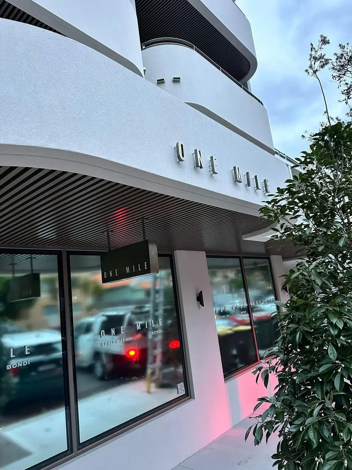 Wide exterior view of ONE MILE facade lettering, projecting lightbox and window branding at Bondi Beach
