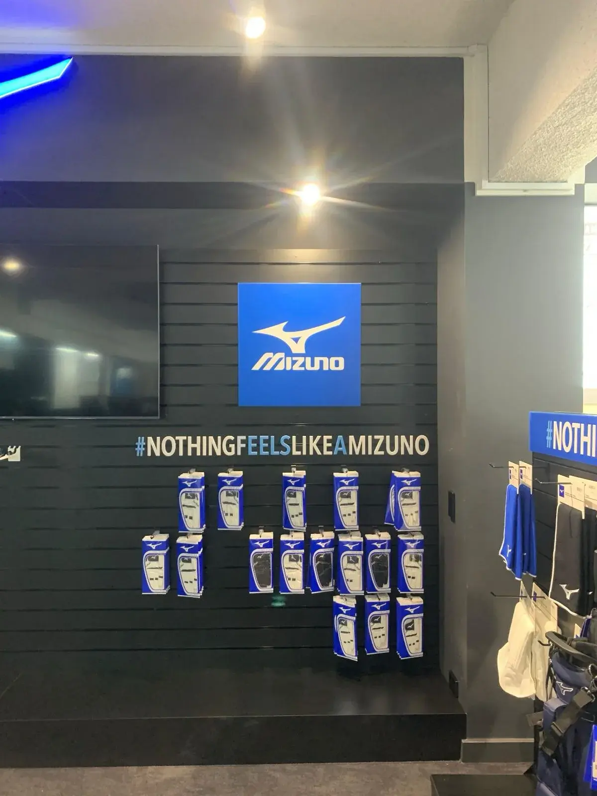Mizuno brand bay with a square logo panel and slogan lettering across the merchandised slat wall