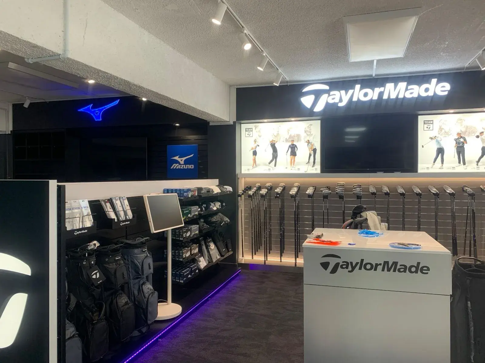 Illuminated TaylorMade department sign with the blue Mizuno logo glowing in the neighbouring bay