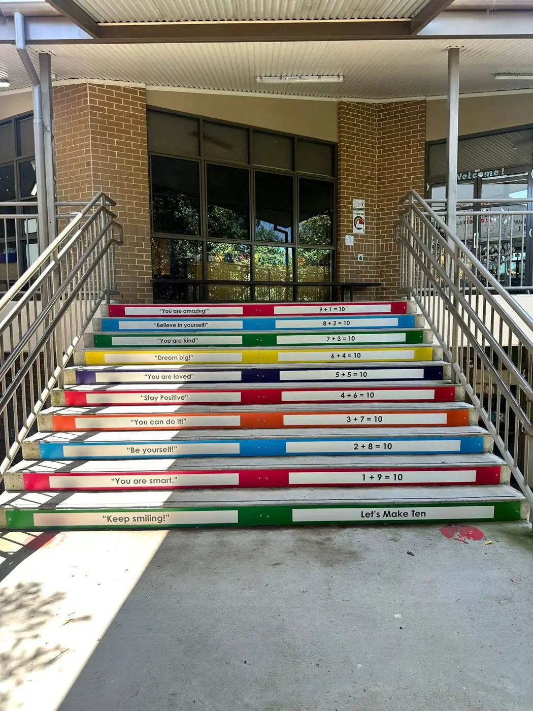 School staircase with rainbow stair graphics showing encouraging phrases and number facts on each riser at St Clare's Catholic Primary School