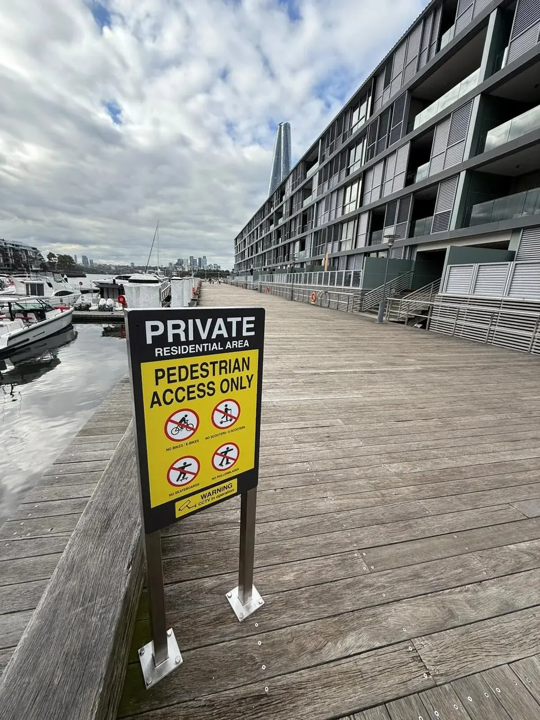 Black private residential area sign and yellow pedestrian access sign installed on the wharf boardwalk beside moored boats