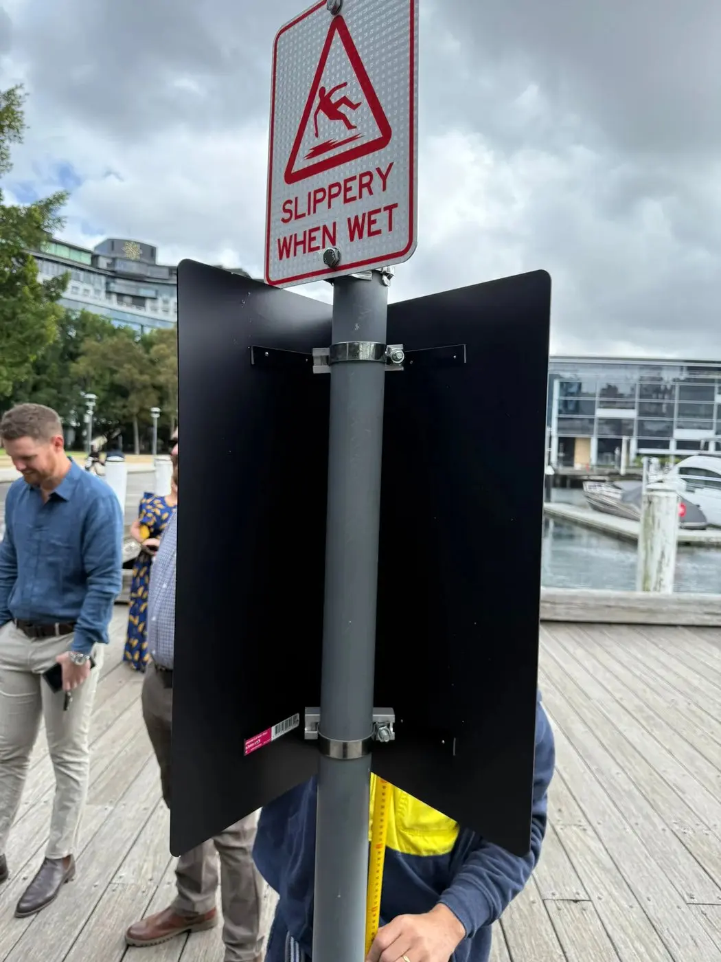 Folded black L-shape sign being fitted around a pole so it reads from both directions of the boardwalk