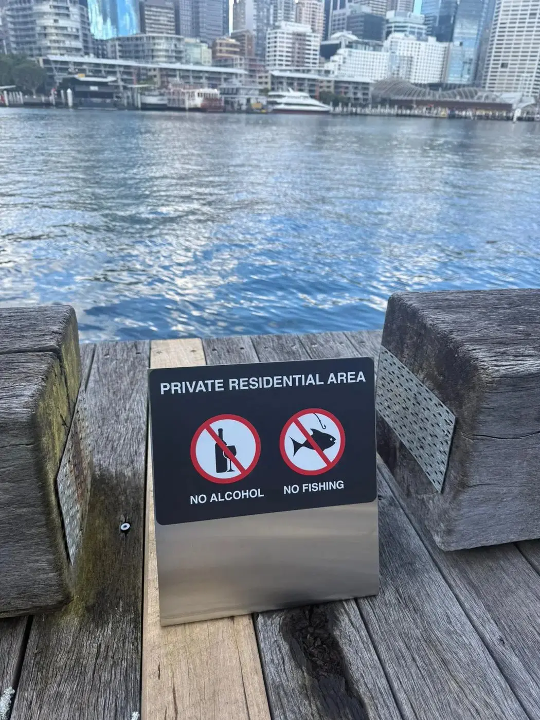 Small private residential area panel mounted at the water's edge with the harbour and city skyline behind