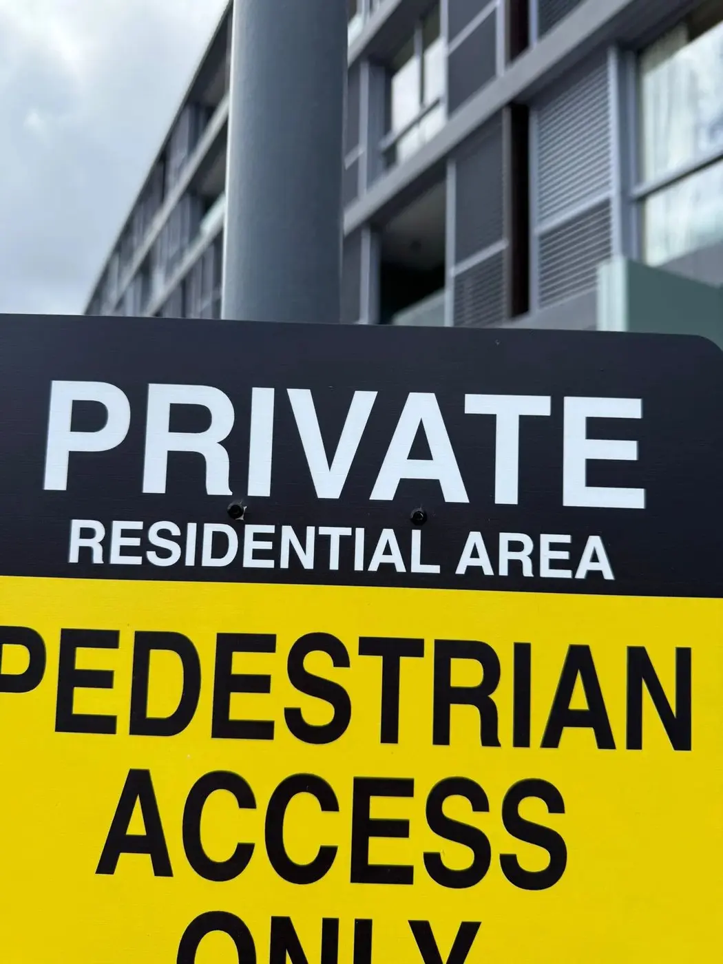 Close view of the black private residential area header over the yellow pedestrian access only panel