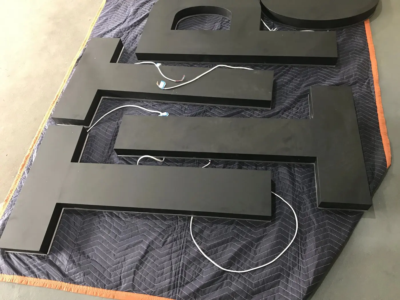 Large black aluminium channel letters spelling TIP laid out on protective blankets with LED wiring visible
