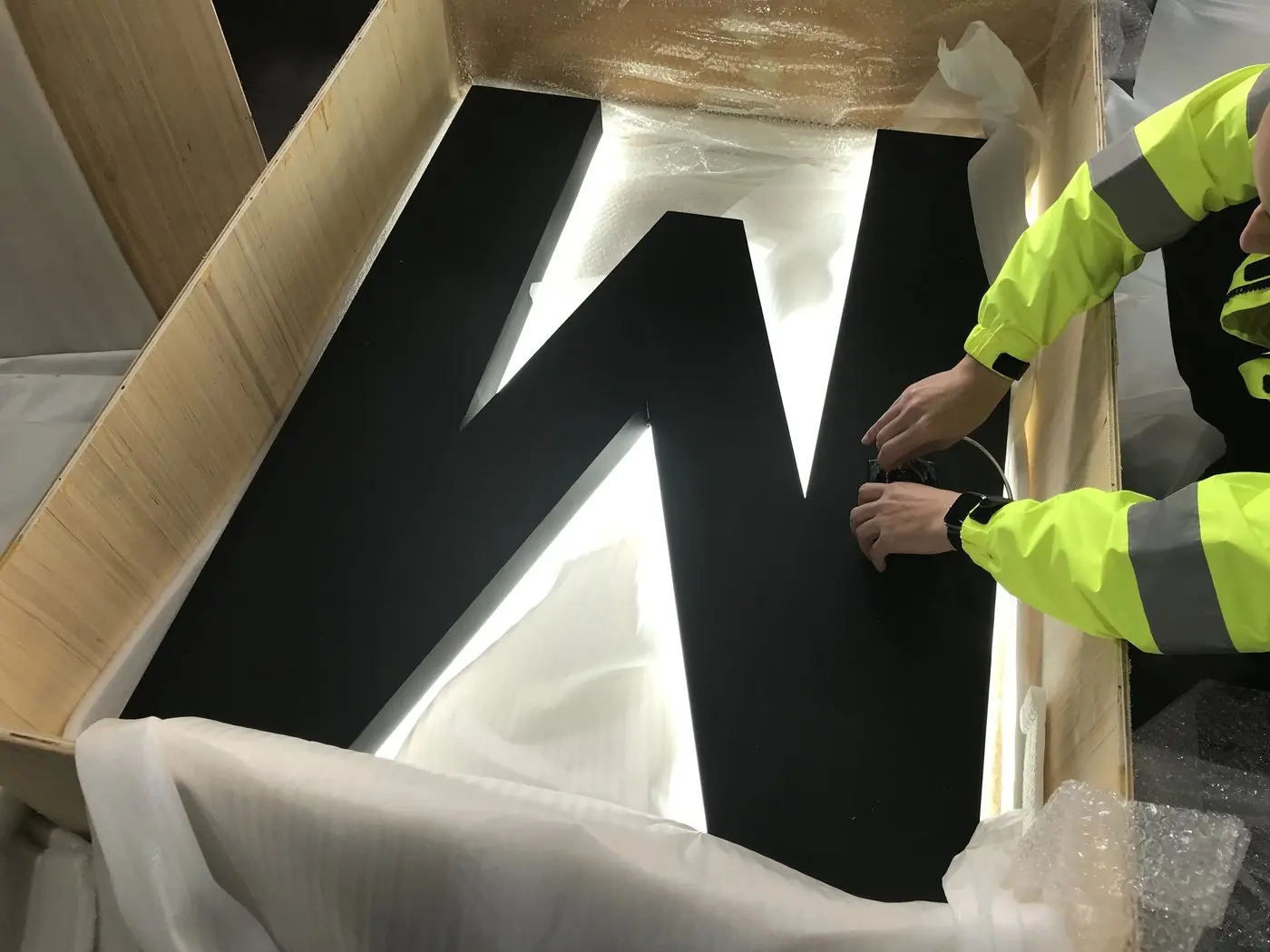 Installer in hi-vis unpacking a letter M taller than an arm span and connecting its LED wiring