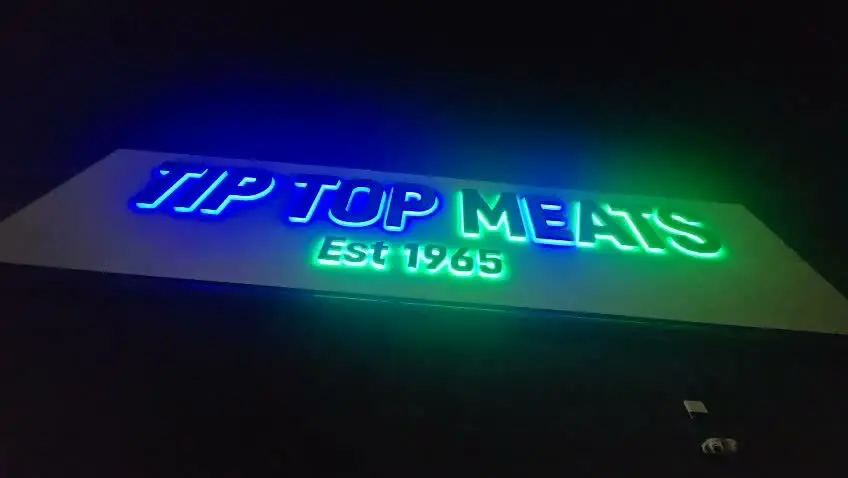 Tip Top Meats sign caught mid-transition with letters fading between blue and green at night