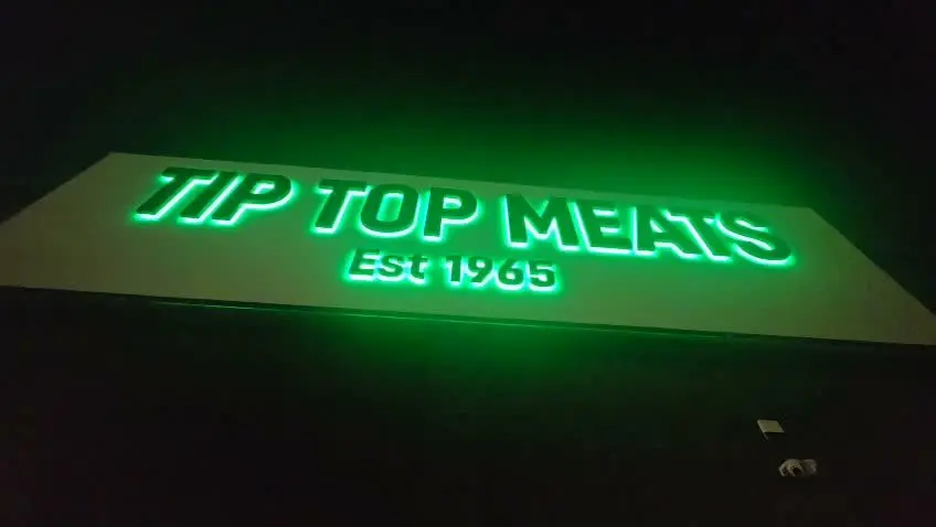 Tip Top Meats halo-lit 3D letters glowing bright green at night after installation