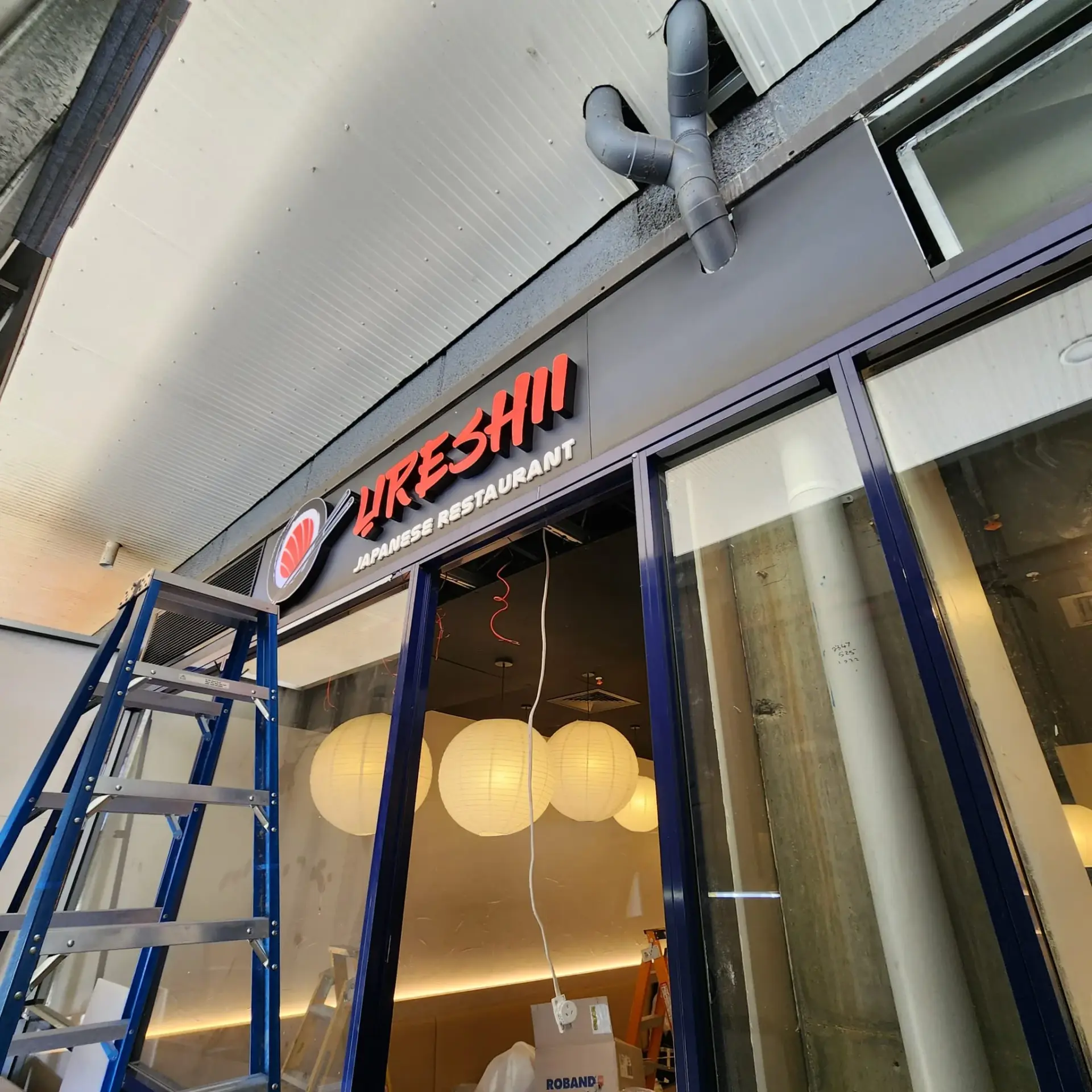 Dimensional orange Ureshii shopfront letters, white restaurant descriptor and sushi logo during installation