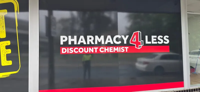 Pharmacy 4 Less logo in red and white on dark shopfront glazing.