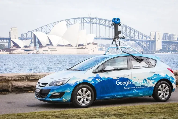 Google Street View car in its printed blue livery with roof camera rig, photographed in front of the Sydney Opera House and Harbour Bridge