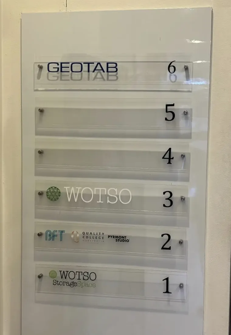 Shared building directory board with six numbered clear acrylic strips, the top strip carrying the Geotab name